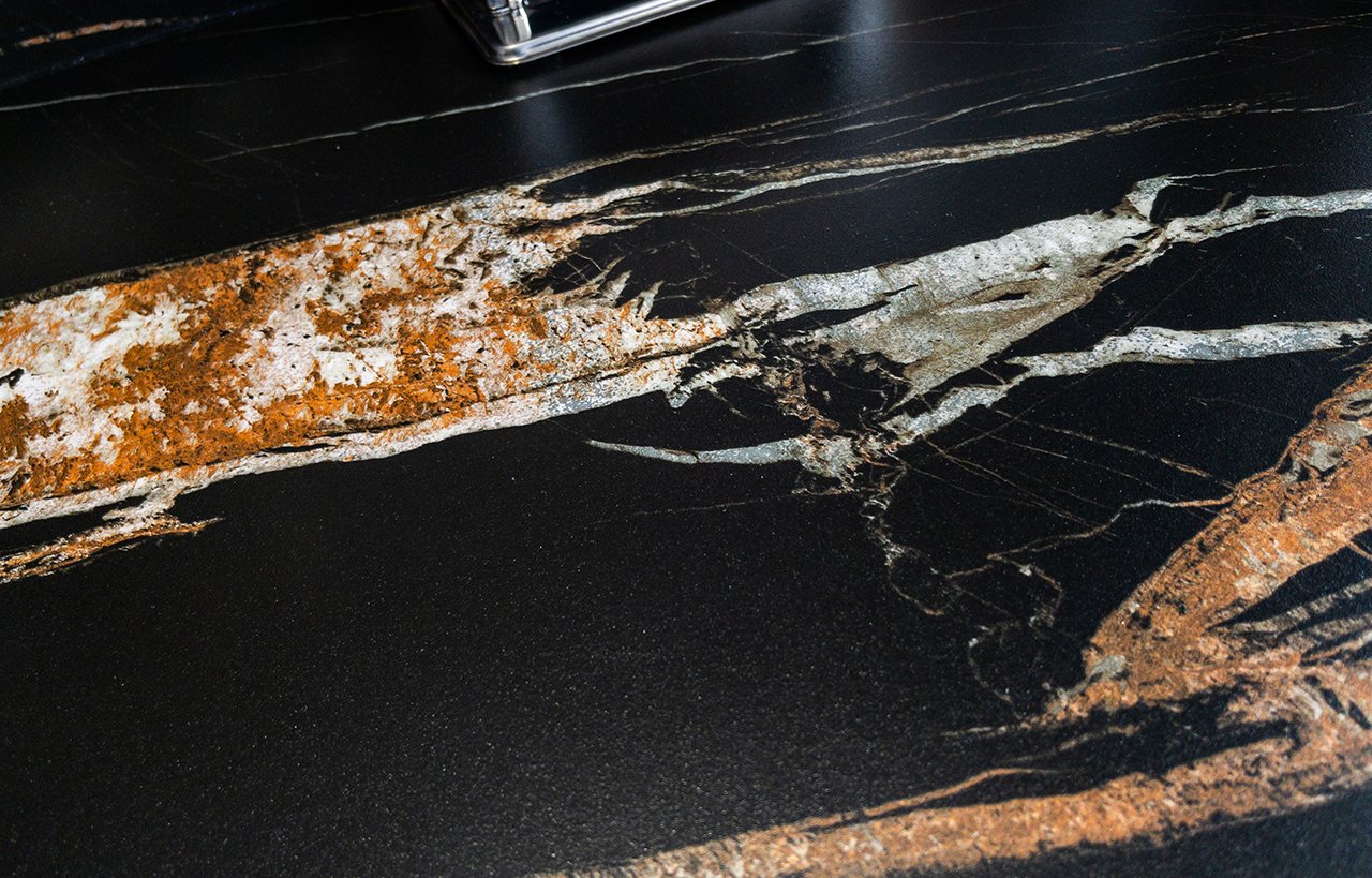 Noir St Laurent Porcelain close-up showing a dramatic amber vein running across a deep black surface near the hob area.