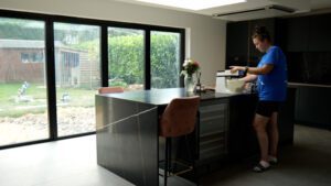 Testimonial kitchen with Sahara Noir Quartz waterfall island showing black surface with gold-toned veining, with Jessica standing beside the island