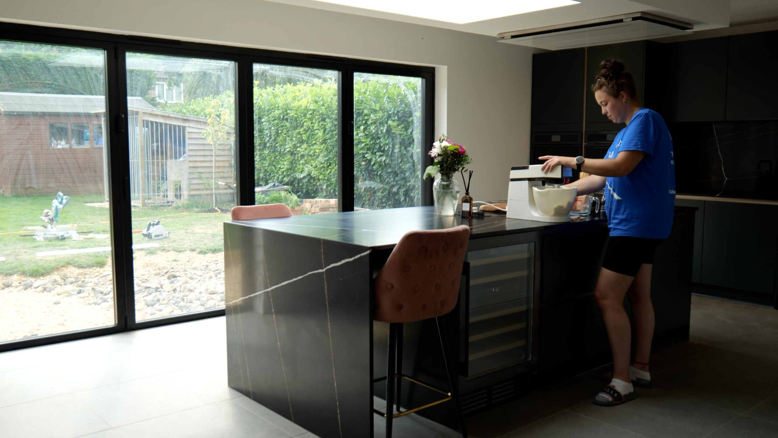 Testimonial kitchen with Sahara Noir Quartz waterfall island showing black surface with gold-toned veining, with Jessica standing beside the island