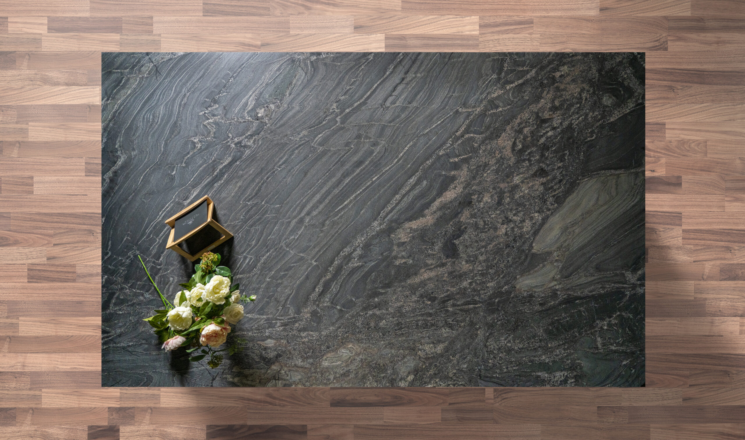 Overhead view of a Black Storm leathered Granite island worktop showing sweeping veining and a textured finish, styled with a small flower arrangement.
