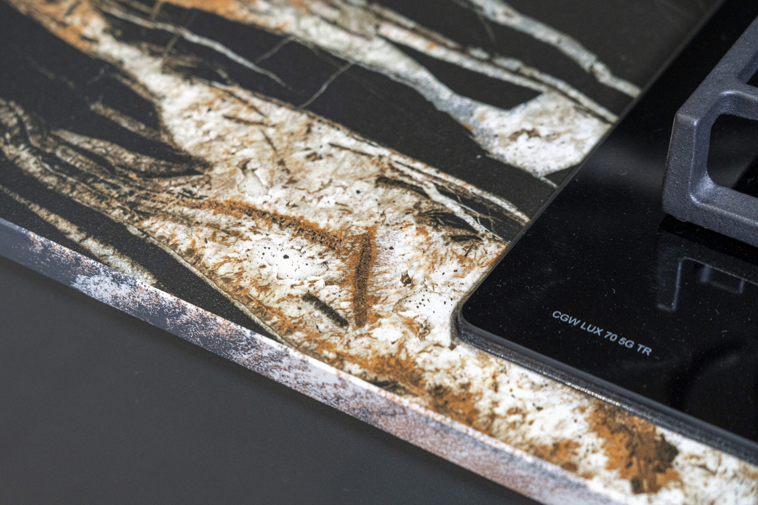 Noir St Laurent Porcelain worktop edge close-up with bold gold, copper and white veining on a deep black surface beside the hob.