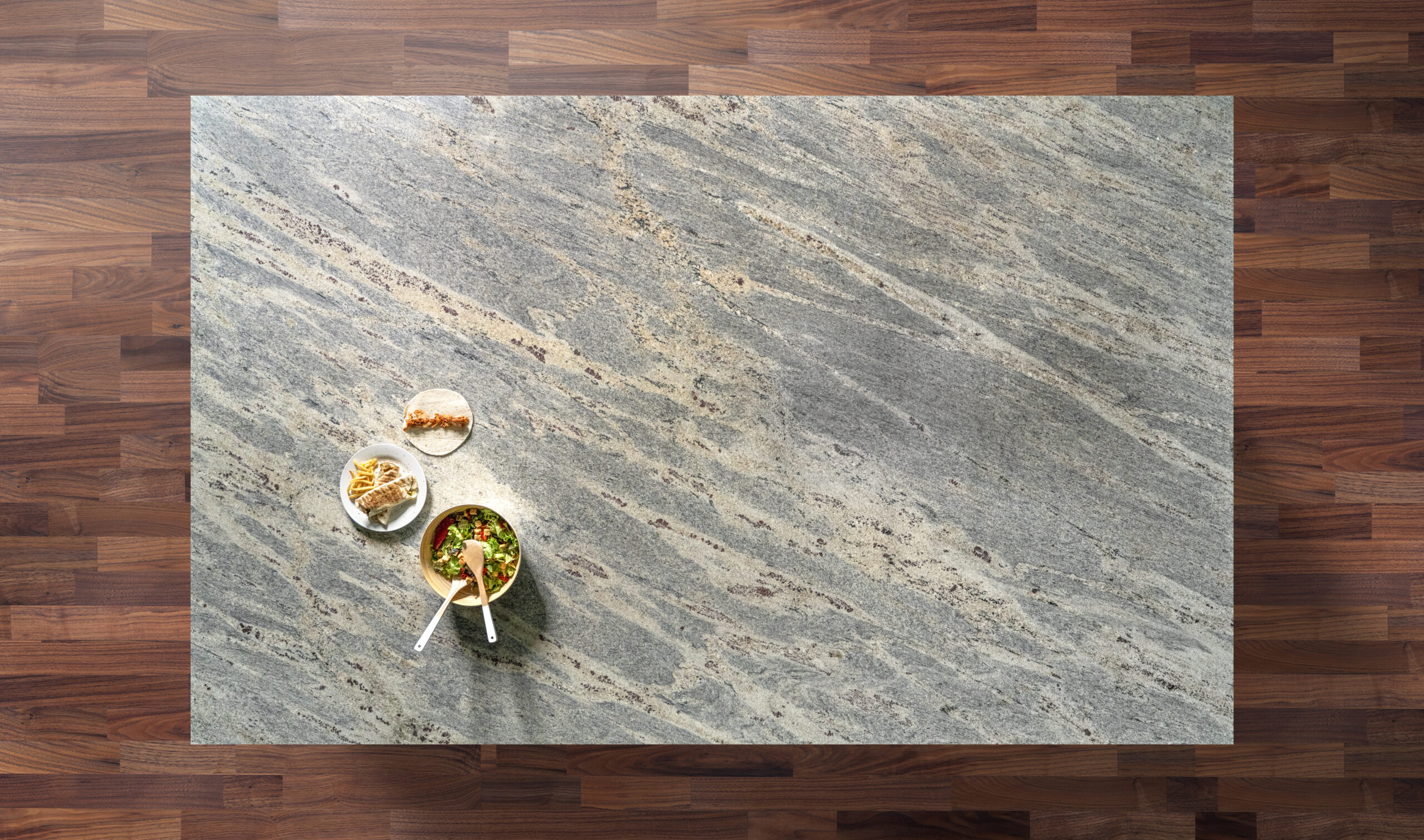 Overhead view of a Kashmir White Granite worktop showing soft grey veining and warm mineral flecks, photographed from above with a small styled tray in the corner.