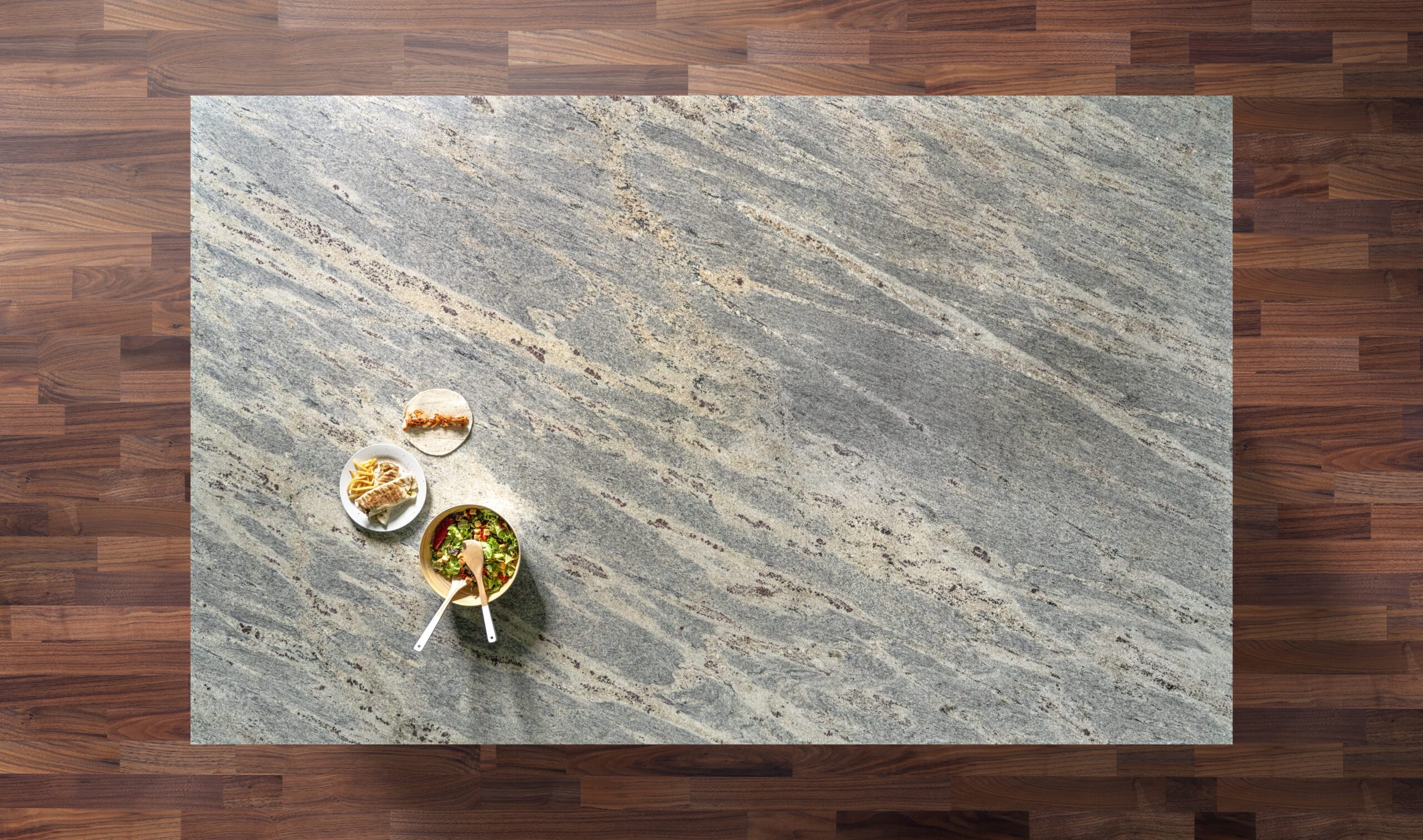 Overhead view of a Kashmir White Granite worktop showing soft grey veining and warm mineral flecks, photographed from above with a small styled tray in the corner.