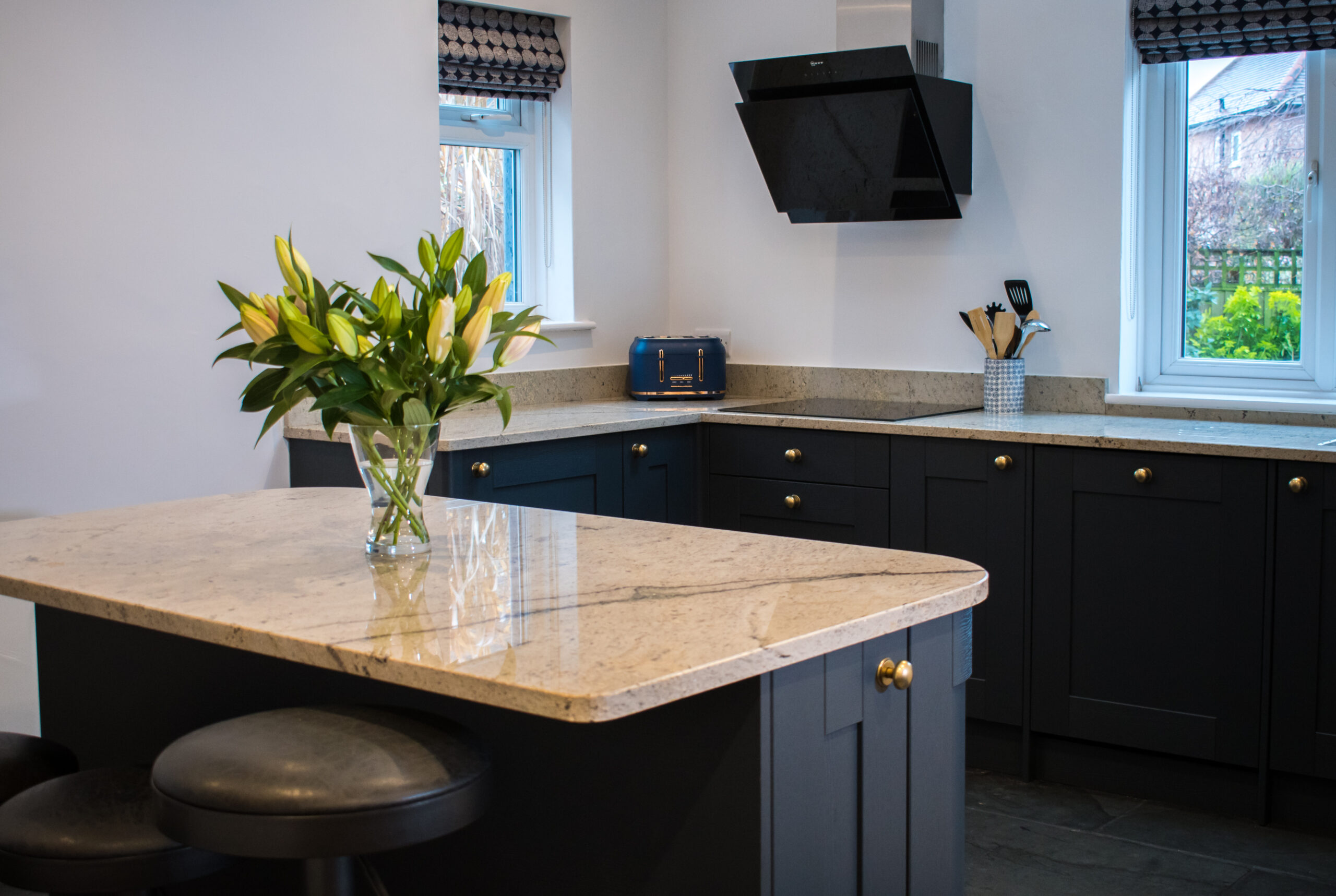 Wide view of an Ivory Spice Granite island worktop with breakfast bar seating, showing the island shape, dark cabinetry and light Granite surface.