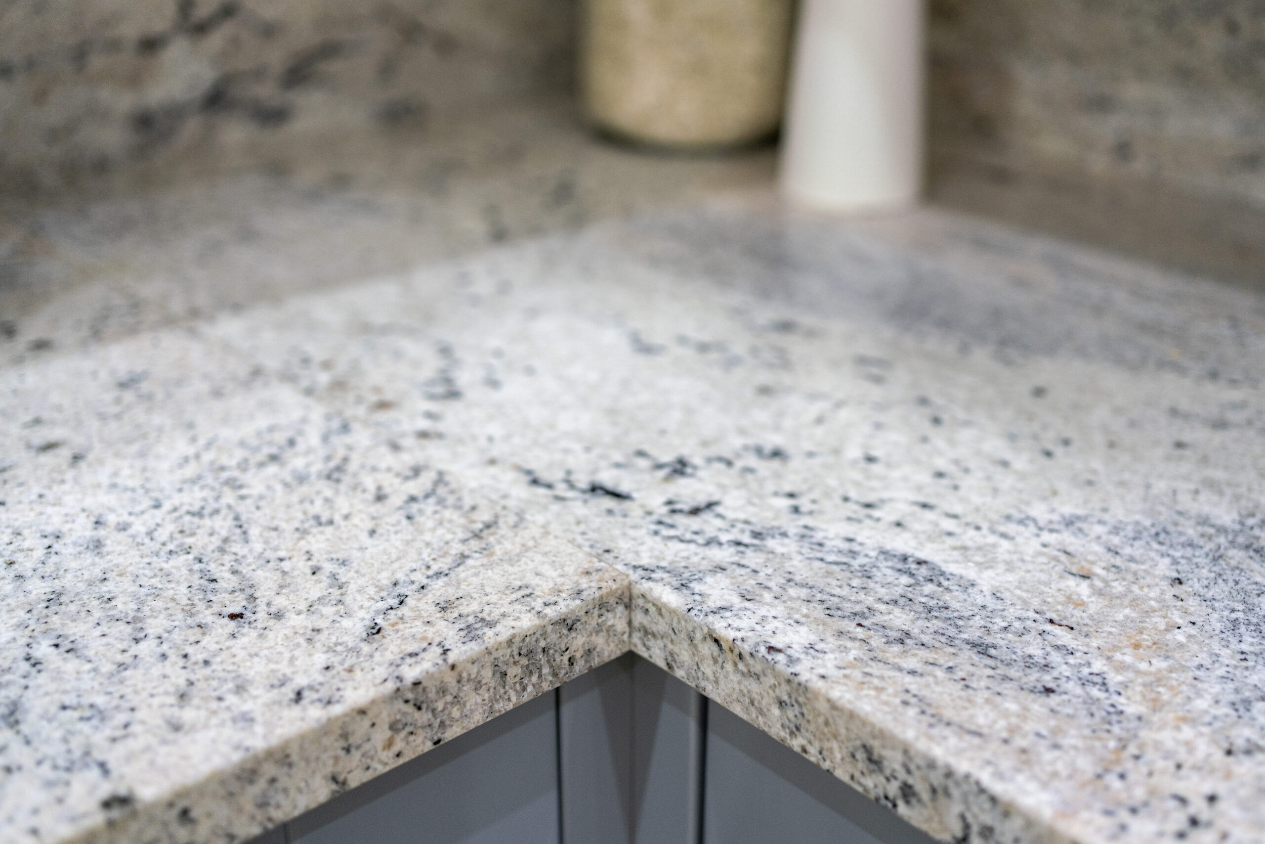 Close up of an Ivory Fantasy Granite worktop corner showing the polished edge detail and natural speckling across the surface.