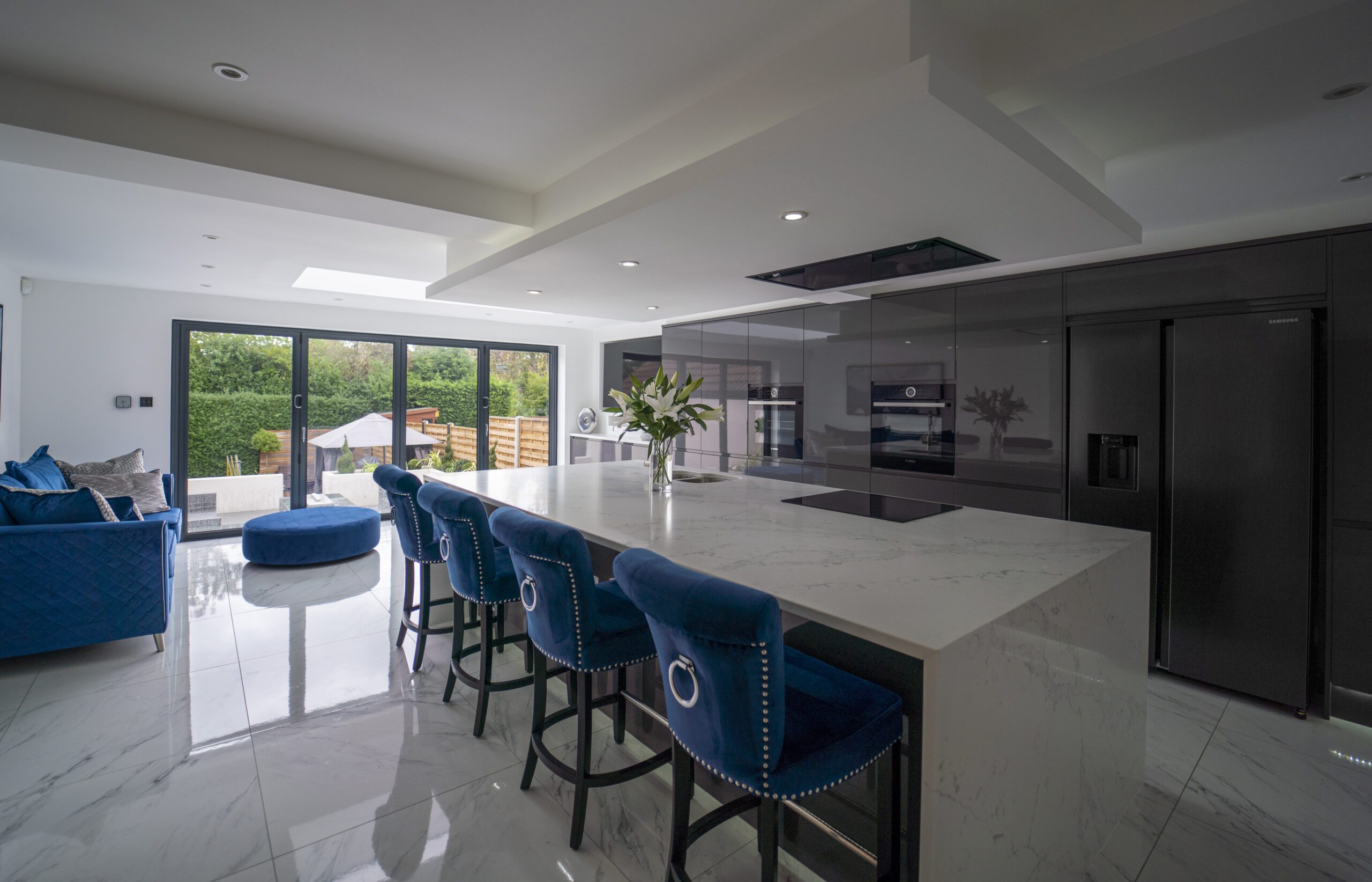 Modern open plan kitchen with White Calacatta Quartz island and blue bar stools under skylights