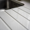 Close-up of Imperial White Quartz drainer grooves beside an inset sink with clean, straight channels