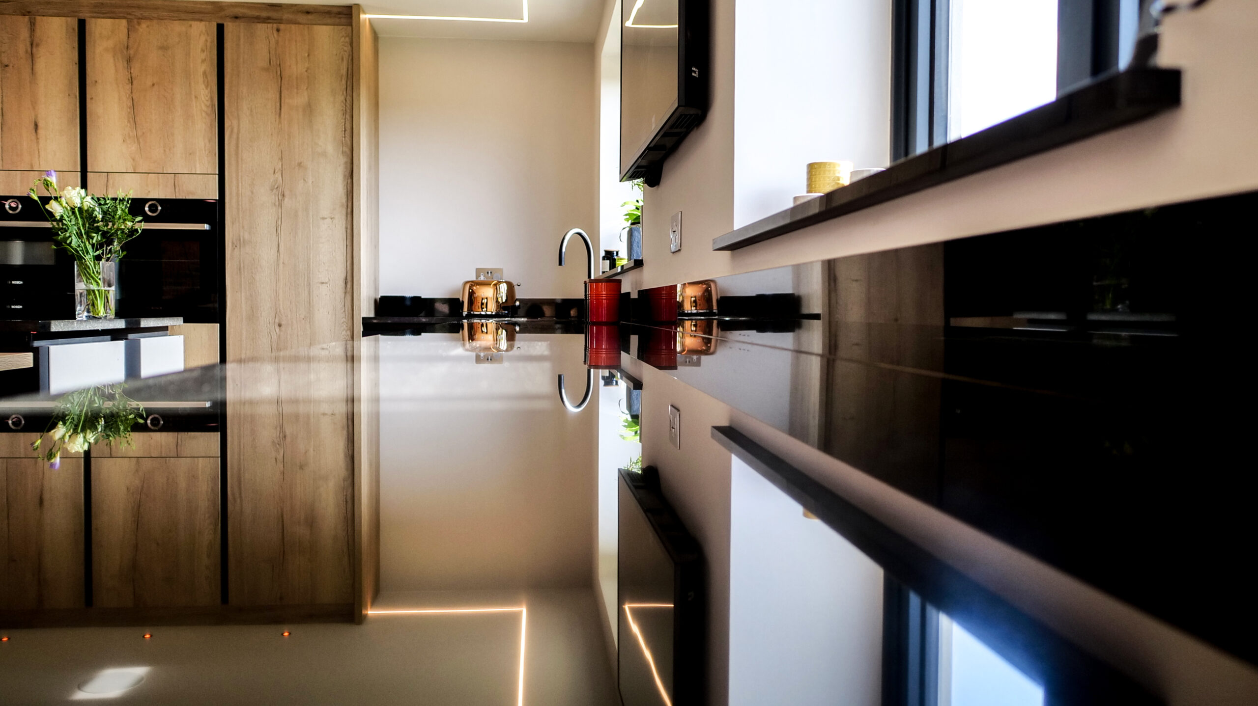 Side view along an Absolute Black Granite island worktop showing the polished edge and overhang, with bottles and glasses styled on the surface.