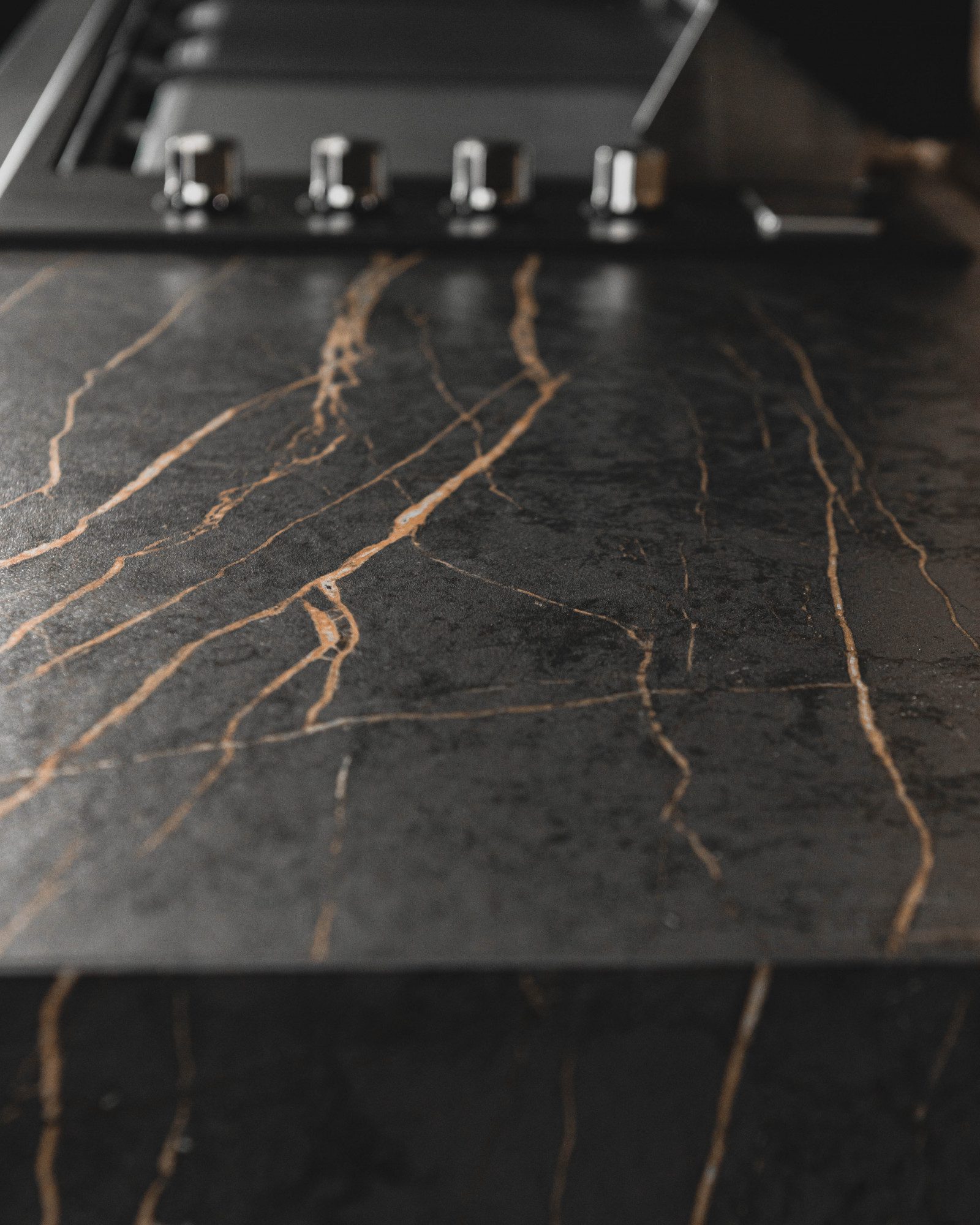 Laurent Porcelain worktop close-up showing dark stone-effect surface with strong gold veining under kitchen lighting.