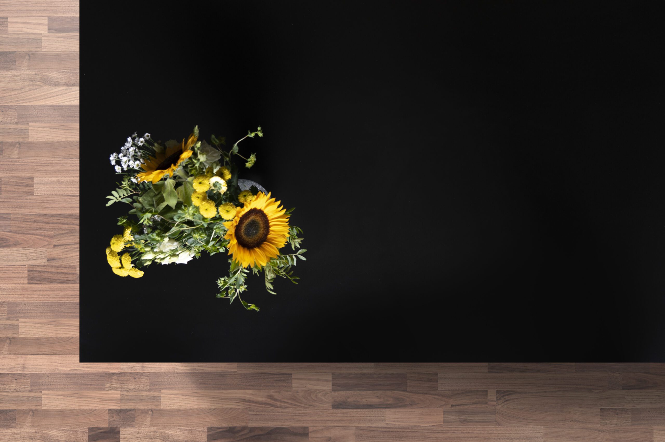 Magma Black Porcelain worktop sample display with a sunflower bouquet on the corner above a wood-effect surface